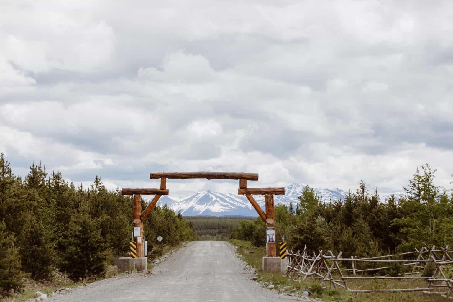 A gravel road running toward the mountains showing a wooden arch in Tŝilhqot’in territory.